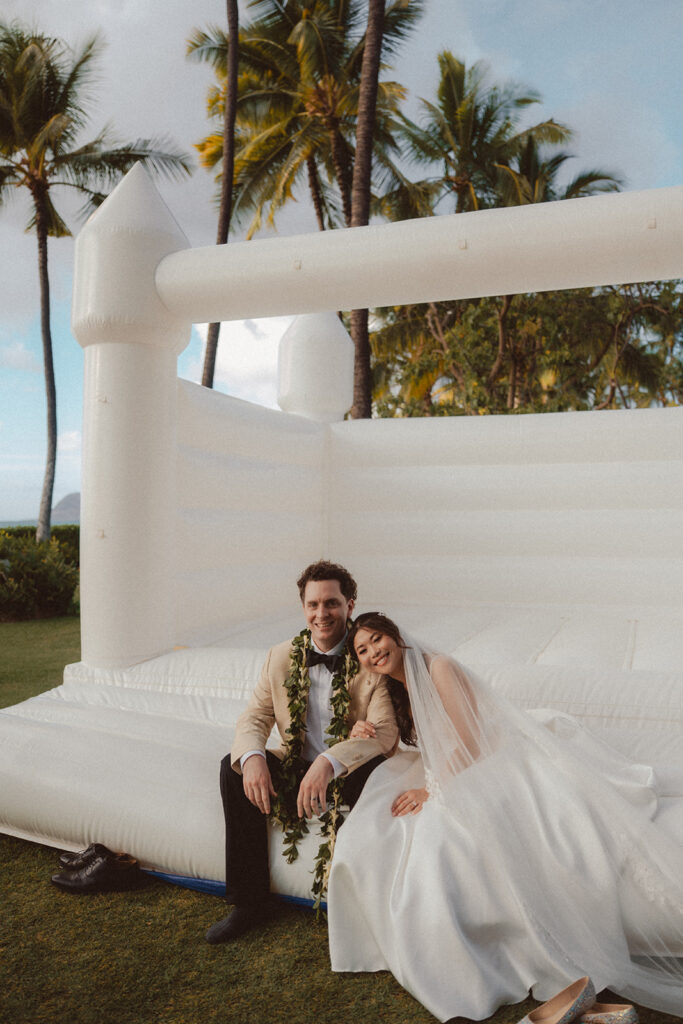 Discover creative wedding reception ideas in Hawaii, including a white bouncy castle, floral champagne tower, and unique guest book ideas from a stunning celebration at Lanikuhonua in Ko Olina, Oahu.